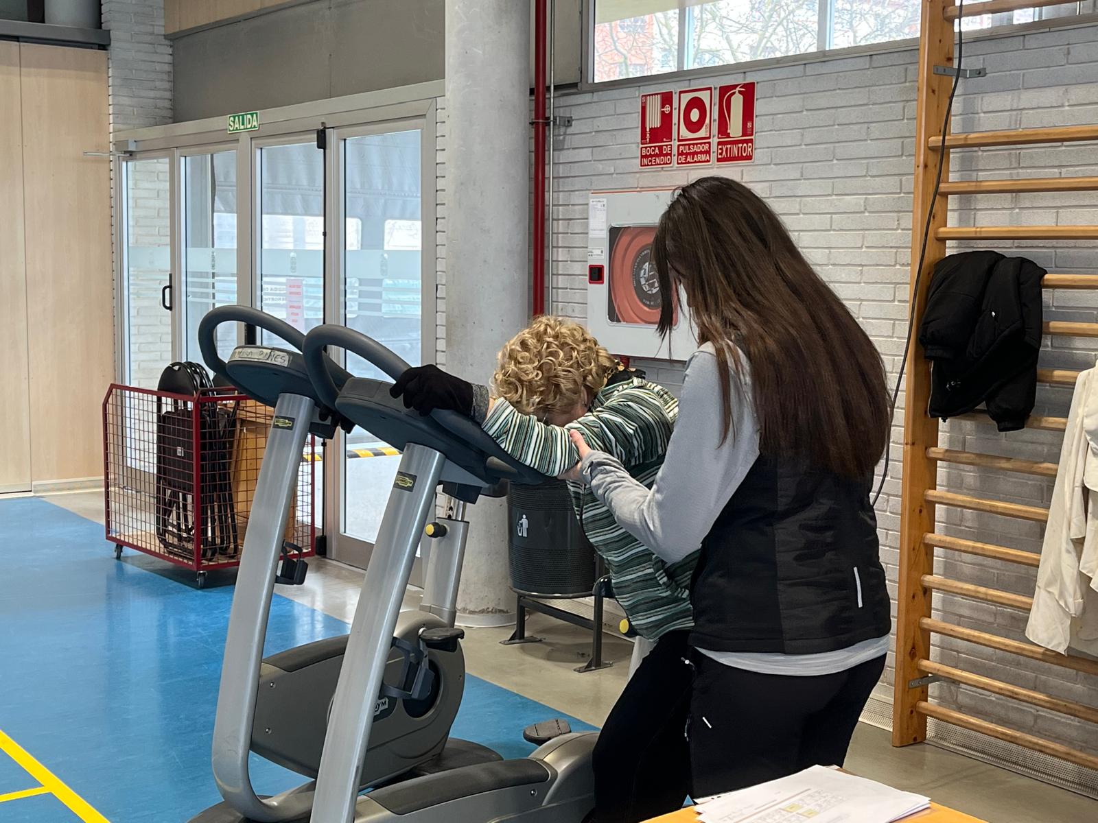 Entrenadora ayudando a participante en bicicleta estática