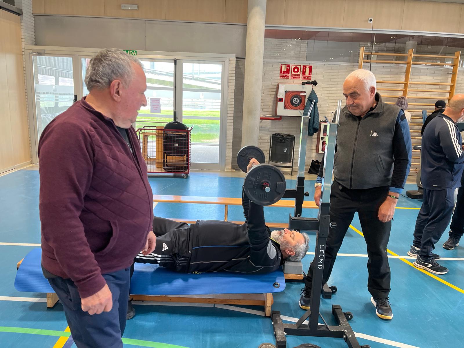 Participante haciendo press de banca con compañeros supervisando