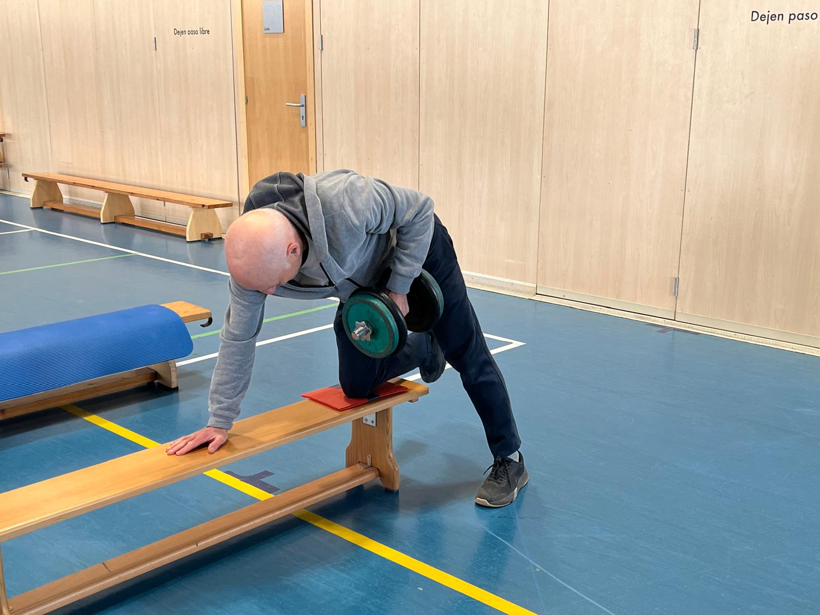 Participante realizando remo con mancuerna en banco